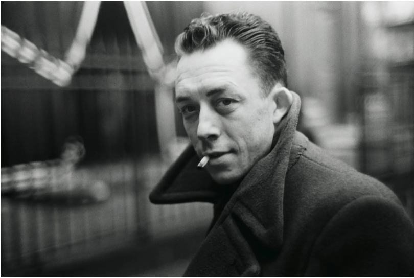 a black-and-white image of philosopher Albert Camus in a heavy coat, looking over his shoulder at the camera